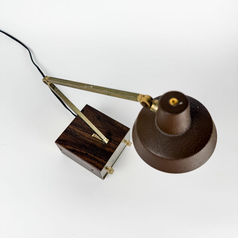 May include: A vintage brown desk lamp with a textured shade and a wooden base. The lamp features an adjustable arm with brass-colored accents and a black power cord. The base is a dark wood cube.