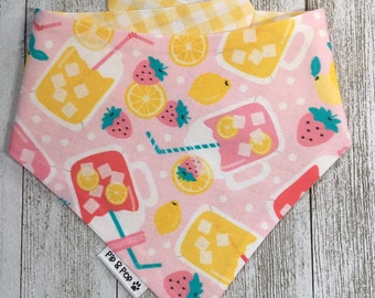 May include: Pink bandana with a yellow and pink lemonade print, strawberries, and lemons. The bandana has a yellow and white gingham trim and a white tag with the text "Pip & Pop" in black.