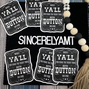 May include: Six black and white stickers with the text "Why Y'all Trying to Test the Beth Dutton in Me" on a black background. The stickers are on a black surface with a white and black beaded garland and a brown tassel.