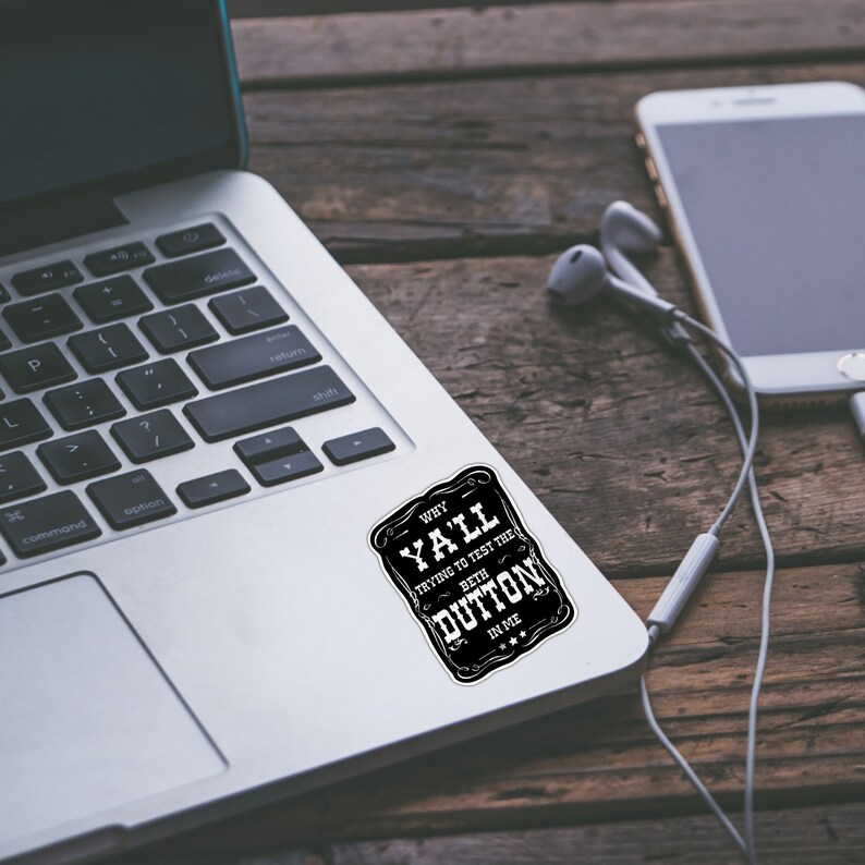 May include: A black and white sticker with the text "WHY YA'LL TRYING TO TEST THE BETH DUTTON IN ME" on a silver laptop.