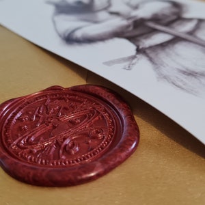 May include: A gold envelope with a red wax seal. The seal has a detailed design. The envelope has a white card attached to it with the text "Within The Story" printed on it.