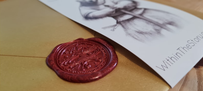 May include: A gold envelope with a red wax seal. The seal has a detailed design. The envelope has a white card attached to it with the text "Within The Story" printed on it.