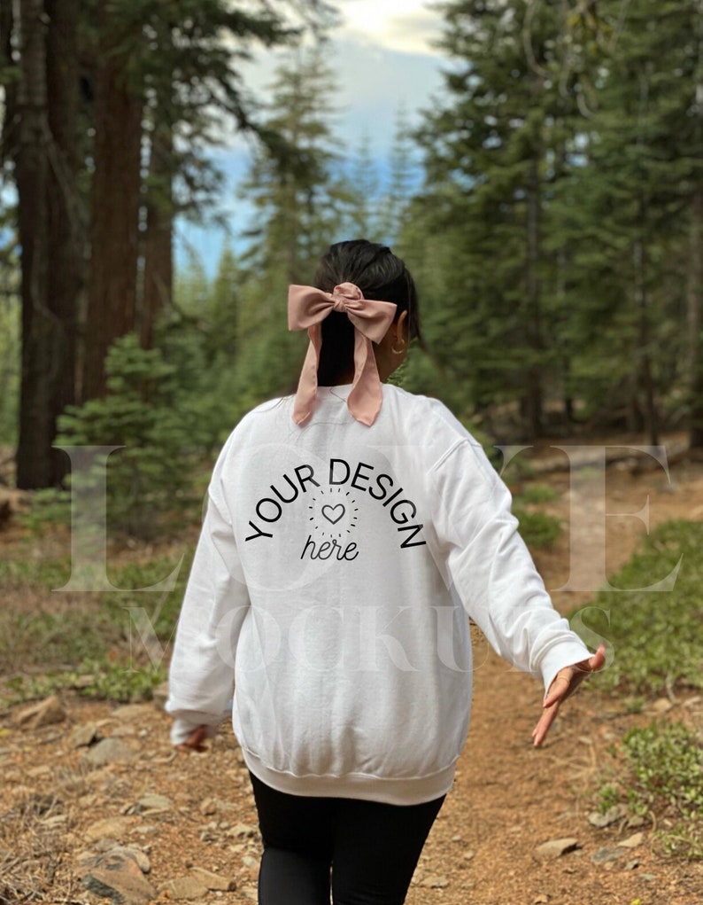 May include: White sweatshirt with a pink bow in the hair of the person wearing it. The sweatshirt has the text "YOUR DESIGN here" with a small heart graphic.