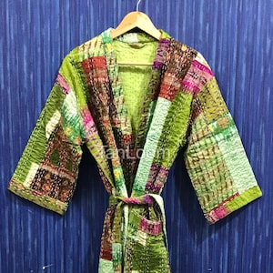 May include: A patchwork robe in shades of green, brown, and pink hangs on a wooden hanger. The robe features a V-neck, wide sleeves, and a matching belt. The fabric appears to be quilted with visible stitching.