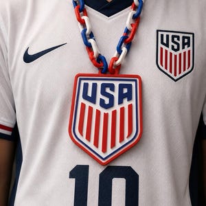 May include: A white soccer jersey with a navy blue Nike swoosh, the USA crest, and the number 10 in navy blue. A large, chunky chain necklace in red, white, and blue links features a prominent USA crest pendant matching the jersey's team logo.