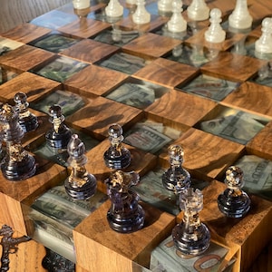 May include: A wooden chessboard with a clear resin top that shows dollar bills underneath. The chess pieces are made of glass and have gold accents. The board is set up for a game of chess.