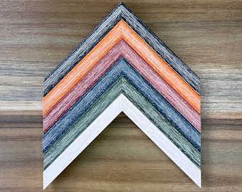 May include: A set of six picture frames in various colors, including white, green, blue, red, orange, and black. The frames are arranged in a chevron pattern, with the white frame at the bottom.