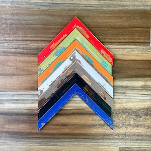 May include: A set of seven wooden picture frames in various colours, including red, orange, yellow, green, blue, grey, and black. The frames are arranged in a chevron pattern, with the largest frame at the top and the smallest frame at the bottom.