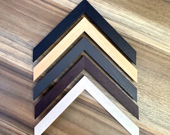 May include: Five different picture frame corners in various colors, including black, brown, white, and two shades of wood. The corners are arranged in a pyramid shape, with the black corner at the top and the white corner at the bottom.
