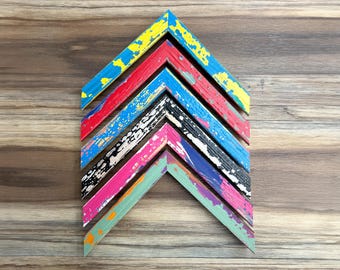 May include: A collection of colorful, distressed wooden picture frames arranged in a chevron pattern. The frames feature vibrant hues of blue, red, black, pink, and green with a weathered, textured finish, set against a wood grain background.