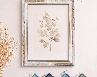 May include: A framed botanical print featuring a single branch with rounded leaves in neutral tones. The frame has a distressed, multi-colored finish. Below the main print, four additional frame corner samples are labeled Ivory, Powder Blue, Black, Ocean Blue, and Green.