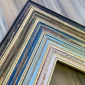 Puede incluir: Un marco de fotos de varias capas con un aspecto desgastado, descolorido y envejecido. El marco est&aacute; hecho de madera y tiene una variedad de colores, incluyendo azul, verde, dorado y rojo. El marco es perfecto para agregar un toque r&uacute;stico y vintage a cualquier decoraci&oacute;n del hogar.