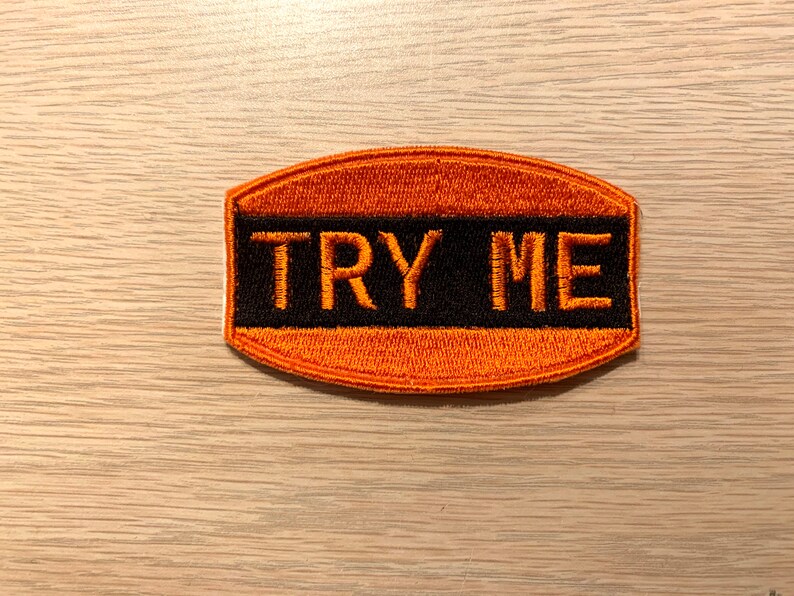 May include: Orange and black embroidered patch with the text "TRY ME" in white.