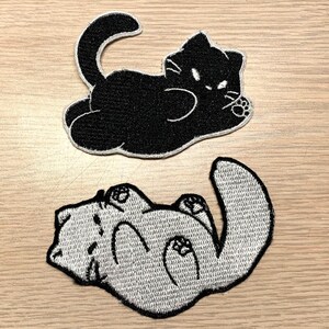 May include: Two embroidered iron-on patches of cats. One is black and the other is white. Both are in a curled up sleeping position.