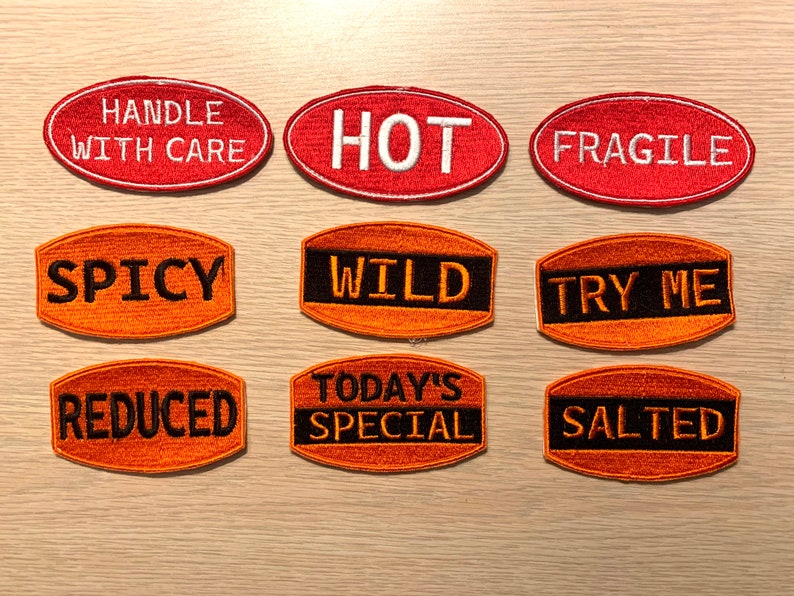 May include: Nine oval-shaped iron-on patches with various phrases, including "Handle With Care", "Hot", "Fragile", "Spicy", "Wild", "Try Me", "Reduced", "Today's Special", and "Salted". The patches are orange and red with black lettering.