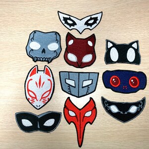 May include: Ten embroidered iron-on patches featuring different masks in various colors, including black, white, red, gray, and blue. The masks are inspired by the popular video game series Persona.