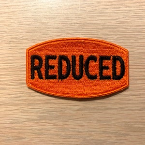 May include: Orange fabric patch with the word "REDUCED" embroidered in black thread.