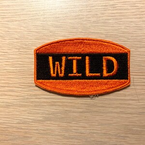 May include: Orange and black embroidered patch with the word "WILD" in orange lettering.
