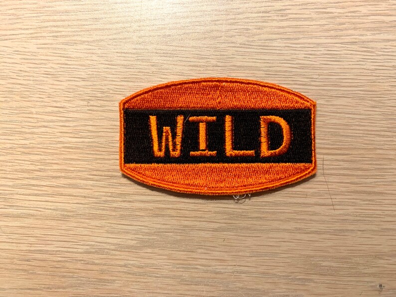 May include: Orange and black embroidered patch with the word "WILD" in orange lettering.