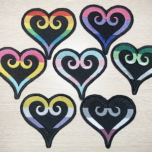 May include: Seven embroidered iron-on patches in the shape of a heart with a swirl design. The hearts are in different colors, including rainbow, pink, blue, green, yellow, and gray.