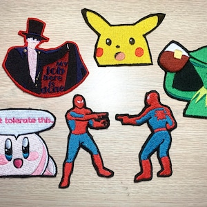 Può includere: Un set di toppe ricamate da stirare con meme di internet popolari. Le toppe includono un Pikachu sorpreso, un Kermit che beve il tè, uno Spiderman che punta un altro Spiderman, un personaggio rosa di Kirby con un fumetto che dice "Non tollererò questo", e un personaggio dell'anime "Sailor Moon" con il testo "Il mio lavoro qui è finito".