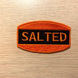 May include: Orange and black embroidered patch with the word "SALTED" in black lettering.