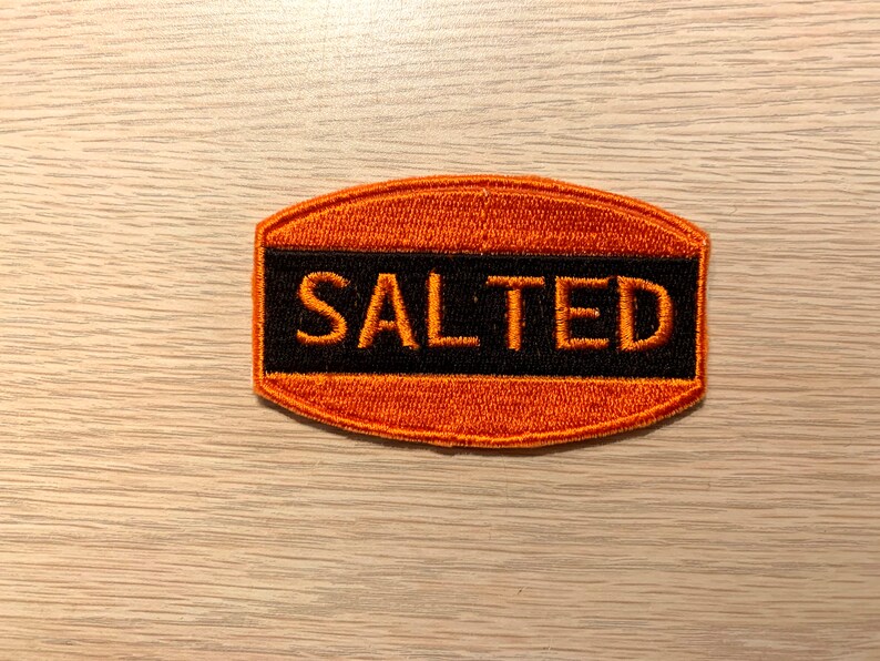 May include: Orange and black embroidered patch with the word "SALTED" in black lettering.