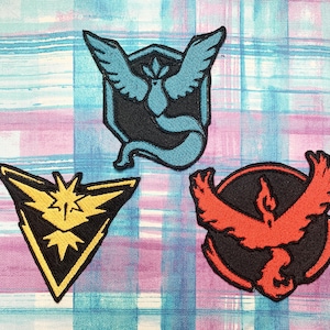 May include: Three embroidered patches featuring the logos of the three legendary Pokemon birds: Articuno, Zapdos, and Moltres. Articuno is blue, Zapdos is yellow, and Moltres is red.