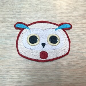 May include: Embroidered owl patch with a surprised expression. The owl has a white face, large black eyes, and a red open mouth. It features blue ear tufts and a red border. This patch is suitable for clothing or accessories.