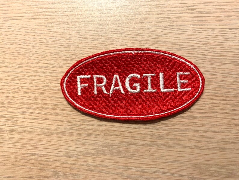May include: Red oval-shaped fabric patch with white embroidered text that reads "FRAGILE".