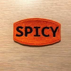 May include: Orange embroidered patch with the word "SPICY" in black lettering.