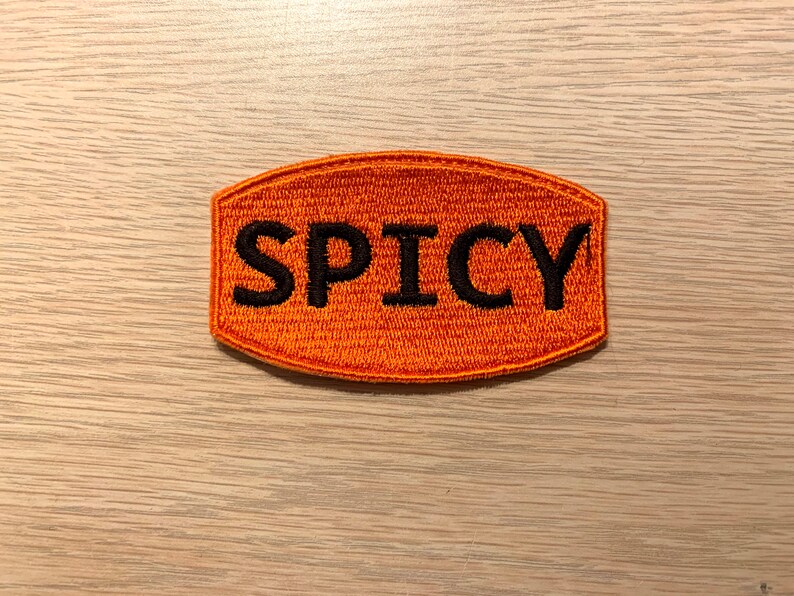 May include: Orange embroidered patch with the word "SPICY" in black lettering.