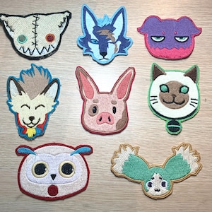 May include: A collection of nine embroidered patches featuring various cartoon animal faces. The patches include a stitched-together doll head, a wolf, a purple creature, a smiling wolf-like character, a pig, a cat, an owl, and a stylized owl.