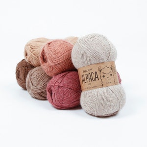 May include: A collection of six balls of yarn in various shades of brown, pink, and beige. The yarn is labelled "DROPS ALPACA MIX".