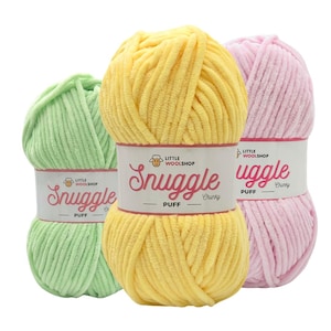 Op de afbeelding: Drie bollen garen in groen, geel en roze. Elke bol heeft een label met de tekst "Little Wool Shop" en "Snuggle Puff Chunky".