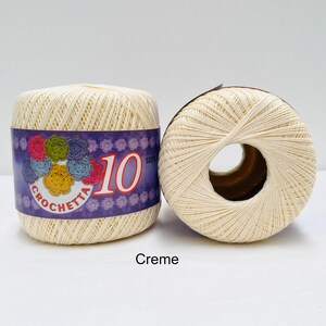 May include: Two spools of cream colored crochet thread. The spool on the left has a purple label with the text "Crochetta 10 100% Cotton".