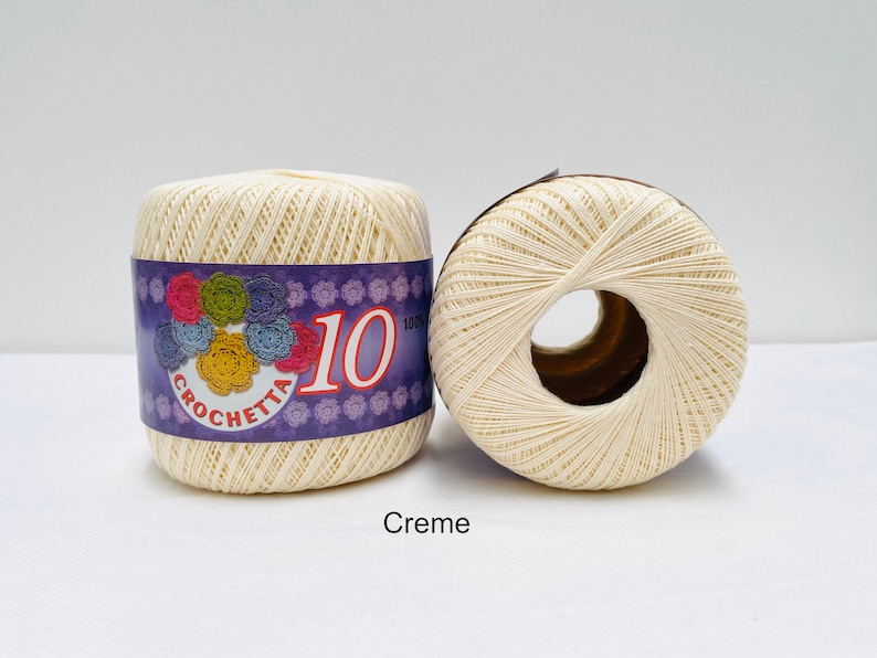 May include: Two spools of cream colored crochet thread. The spool on the left has a purple label with the text "Crochetta 10 100% Cotton".