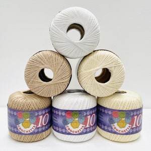 May include: Six balls of yarn in a pyramid shape. The balls are white, beige, and a light brown color. The balls have a label that says "Crochetta 10" with a floral design.