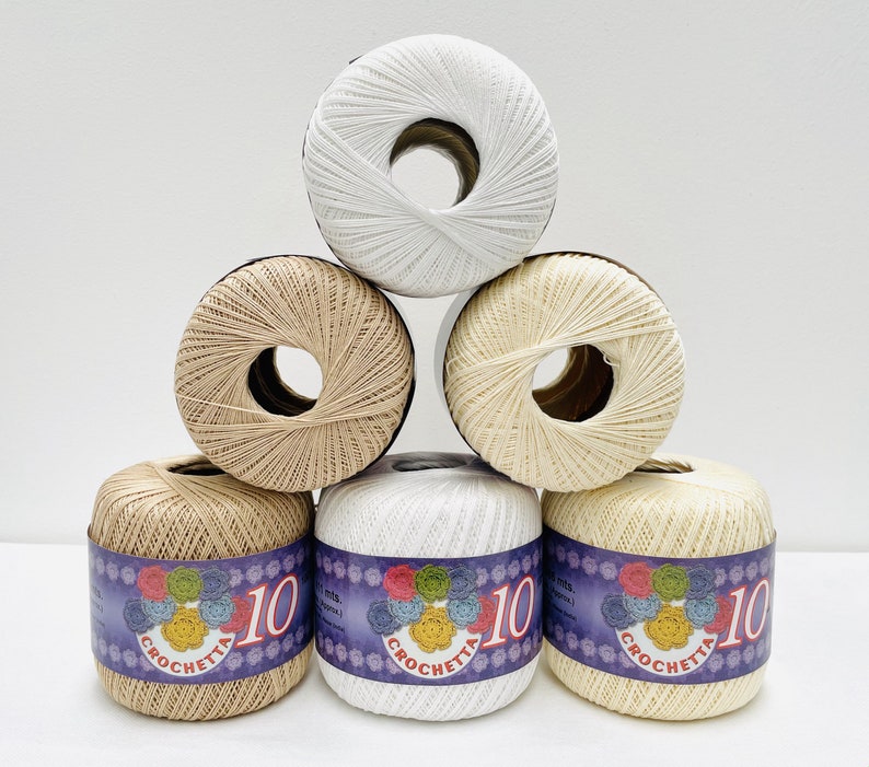 May include: Six balls of yarn in a pyramid shape. The balls are white, beige, and a light brown color. The balls have a label that says "Crochetta 10" with a floral design.
