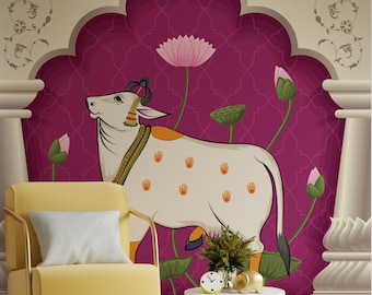 May include: A decorative wall mural featuring a stylized white cow with orange handprints, adorned with jewelry and a peacock feather. The cow is set against a magenta backdrop with lotus flowers and a floral archway. A yellow armchair and side table are in the foreground.