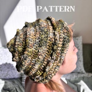 Puede incluir: Un gorro de ganchillo hecho a mano en tonos tierra de verde, marrón y amarillo. El gorro tiene una textura acanalada y un ajuste holgado. El texto "PDF PATTERN" se muestra en blanco.