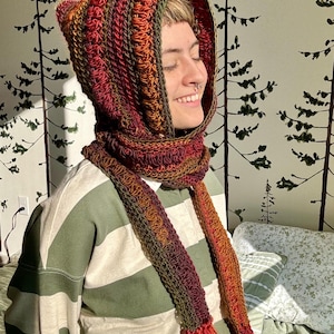 May include: A crocheted hooded scarf with a long fringe. The scarf is made in shades of red, orange, and green.
