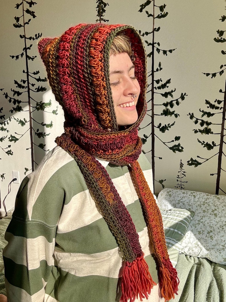 May include: A crocheted hooded scarf with a long fringe. The scarf is made in shades of red, orange, and green.