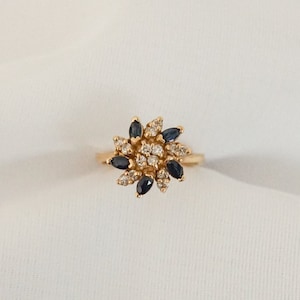 May include: A gold ring with a flower-shaped design featuring blue and white gemstones.