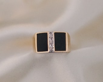 May include: A gold ring with a black rectangular stone and a row of clear stones set in the center.