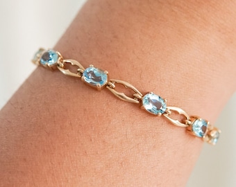 May include: A gold bracelet with oval-shaped blue gemstones. The bracelet is on a person's wrist.