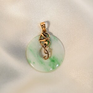 May include: A green jade pendant with a gold swirl design. The pendant is round and has a white background with green swirls.