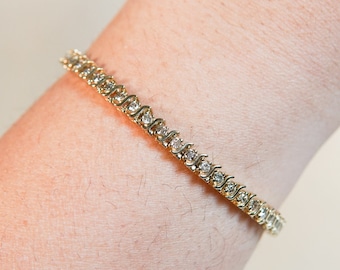May include: A gold tennis bracelet with small round clear stones.