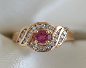 May include: A gold ring with a pink oval gemstone surrounded by smaller diamonds. The ring has a twisted band.