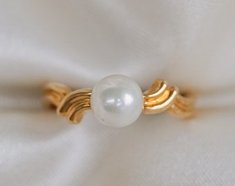 May include: A gold ring with a wavy design and a white pearl in the center.